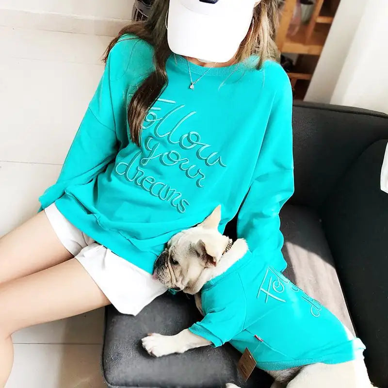 Person wearing a teal sweatshirt with 'Follow Your Dreams' text, sitting on a couch with a dog.